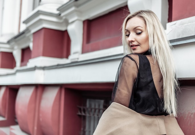 Cute attractive fashion woman in autumn coat posing against the background of urban architecture. Street fashion