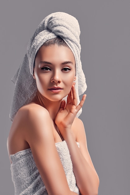 Cute attractive girl with towel on her head isolated on gray background. Skin care concept.