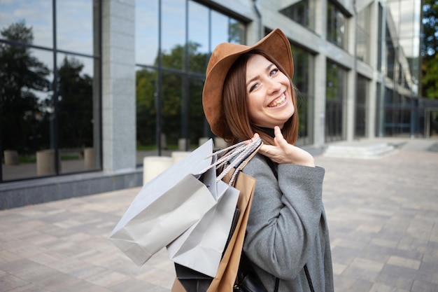 写真 秋のコートと帽子のかわいい魅力的な幸せな買い物中毒の女性は、多くの紙の買い物袋を持っています。