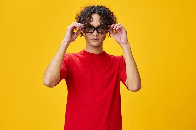 Cute attractive myopic young student man in red tshirt hold funny eyewear posing isolated on over yellow studio background the best offer with free place for advertising education college concept