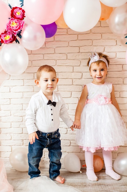 Cute babies - boy and girl are holding hands around the balloons. The baby boy is looking at his girlfriend with enthusiasm