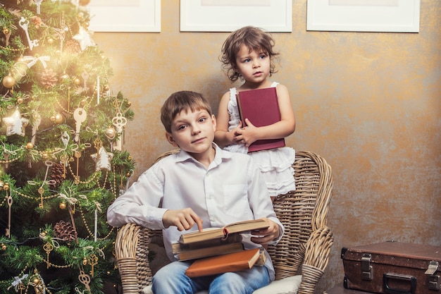 Cute babies boy and girl in a chair reading a book in a Christmas retro interior