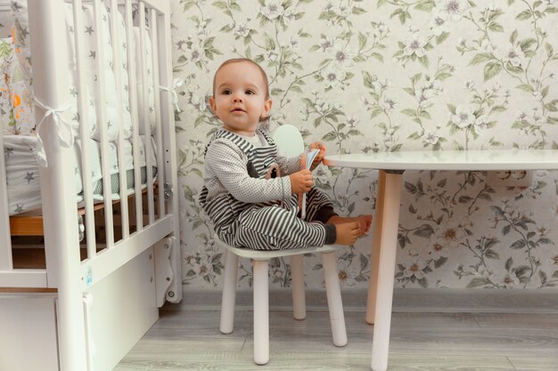 Cute baby 11 months old sits on a highchair near the table.