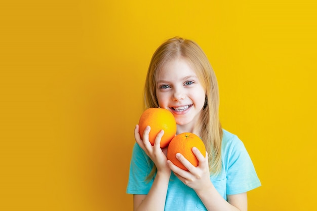 Cute baby 8 years old on an orange wall, blonde pretty girl with appelsins in her hands smiles