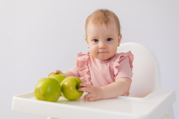 아기 의자 에 앉아 있는 귀여운 아기 가  바탕 에 사과를 어 먹는다