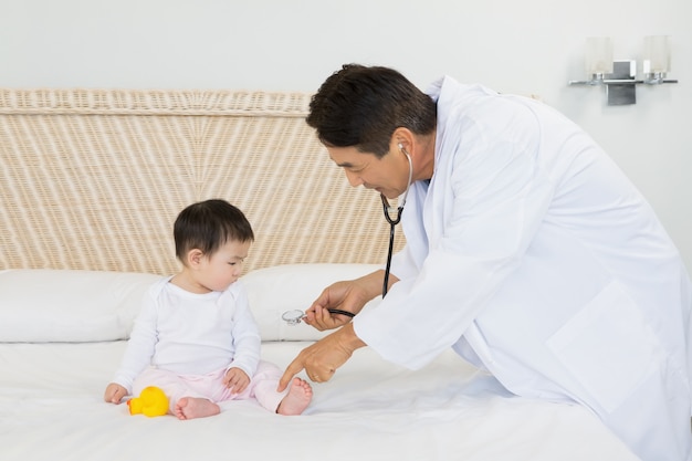 Cute baby being visited by doctor on the bed