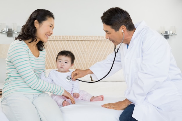 Cute baby being visited by doctor on the bed