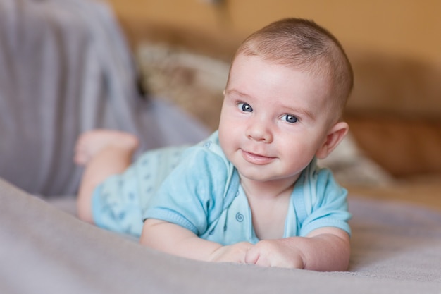 Cute baby in blue clothes lying on the couch and smiling.