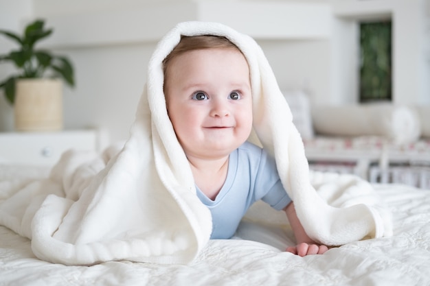 Photo cute baby boy 6 months old in blu bodysuit smiling and lying on bed with white plaid at home.