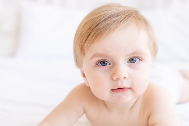 Cute baby boy blonde with big eyes closeup or portrait in the crib at home the concept of baby products and accessories