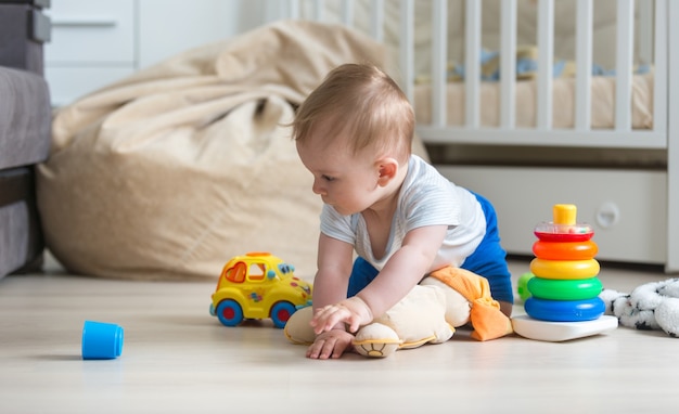 Cute baby boy crawling on floor and playing with toy car