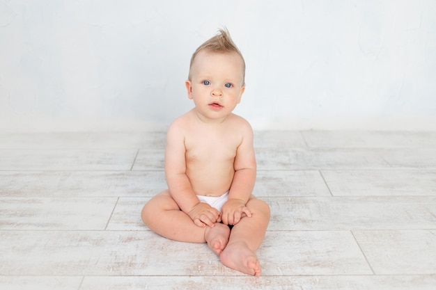 Cute baby boy in diapers on a white background with a hairstyle and big blue eyes smiles