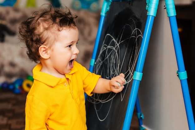 Cute baby boy drawing with chalk on a blackboard