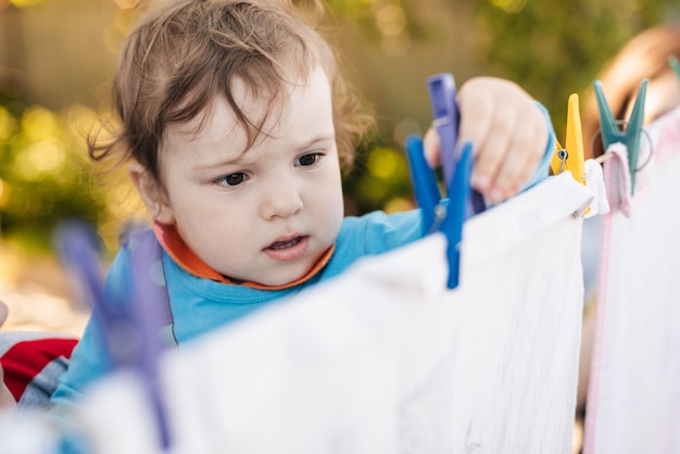 かわいい男の子が洗濯はさみで洗濯物をロープに吊るすのを手伝う