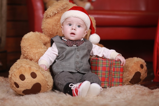 写真 大きなテディベアとクリスマスプレゼントとサンタの帽子のかわいい男の子。