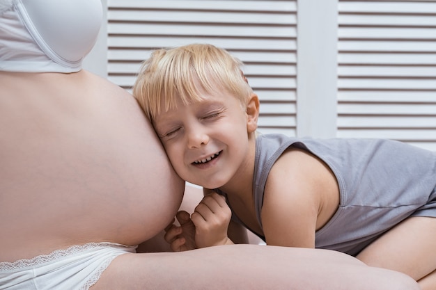 Foto il neonato sveglio ha appoggiato l'orecchio alla pancia della madre incinta e ascolta. secondo concetto di gravidanza.