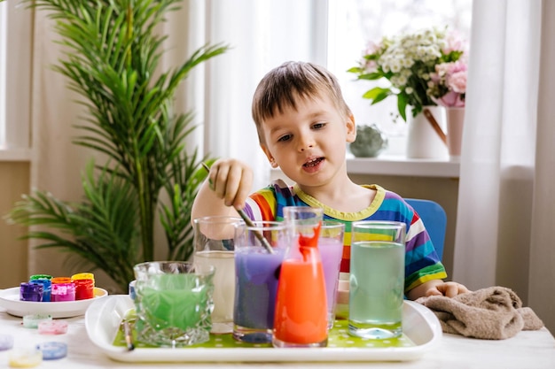 写真 コンテナの初期の開発で水と塗料と異なる色を混合することを学ぶかわいい男の子