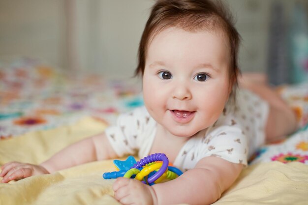 Cute baby boy lying on the bed and play with his colorful toys