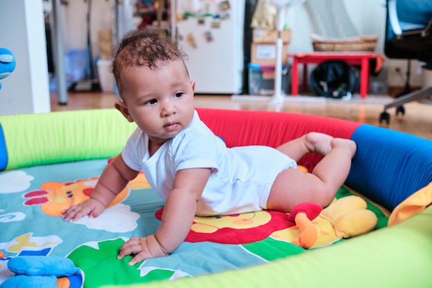 Cute baby boy lying on his tummy on a colorful play mat at home.