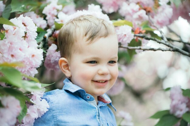 Cute baby boy among pink blossoming flowers