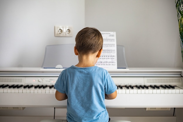 Cute baby boy playing white electrical forte piano pressing keys kid studying at musical school