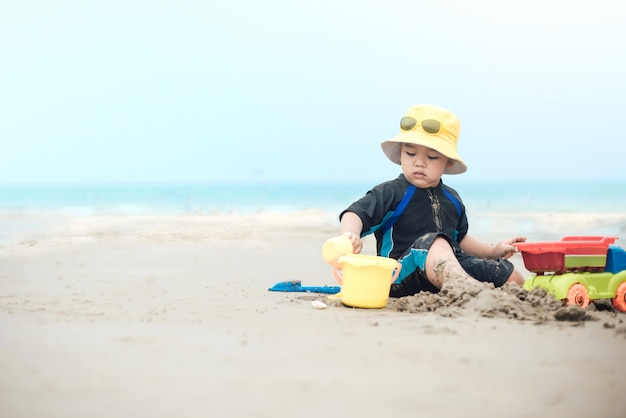 Foto neonato sveglio che gioca con i giocattoli della spiaggia sulla spiaggia tropicale