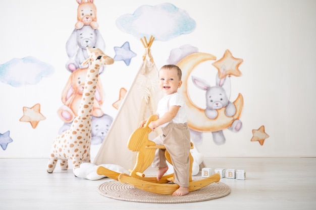 Cute baby boy rides a wooden rocking hare in the children's room at home educational toys for children