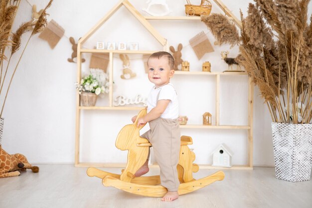 かわいい男の子は、子供のための家庭の教育玩具の子供部屋で木製のロッキング ウサギに乗る