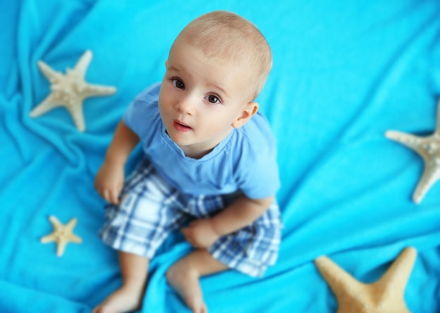 Cute baby boy sitting on bright blanket with sea stars