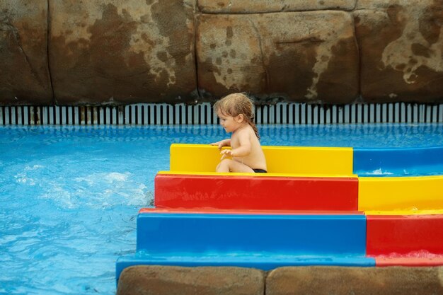 Cute baby boy sliding from colorful waterslide in blue water