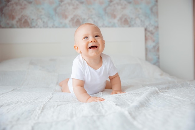 Cute baby boy in a white bodysuit crawling on bed in the bedroom the concept of happy motherhood