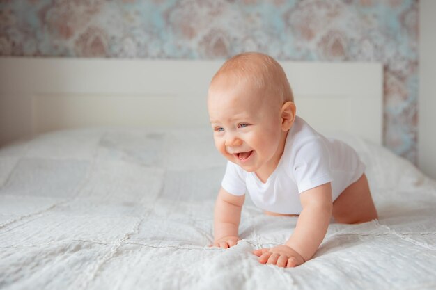 Cute baby boy in a white bodysuit crawling on bed in the bedroom the concept of happy motherhood