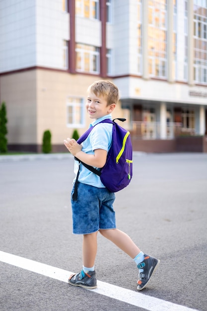 バックパックを持ったかわいい男の子が校庭の小学校の子供の教育の近くに立っています