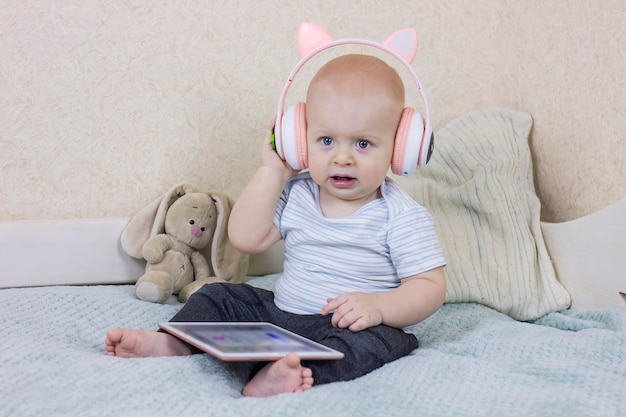 Фото Симпатичный малыш с наушниками и цифровым планшетом очаровательный малыш сидит на диване и слушает музыку