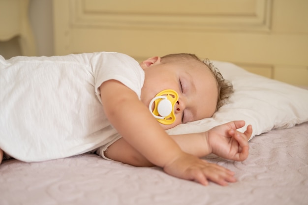 Photo cute baby boy with nipple sleeping on bed at home