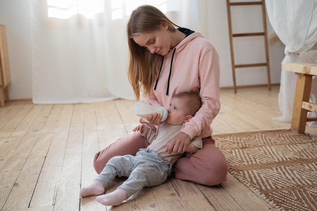 Bambino carino che beve latte dalla bottiglia a casa concetto di alimentazione del bambino