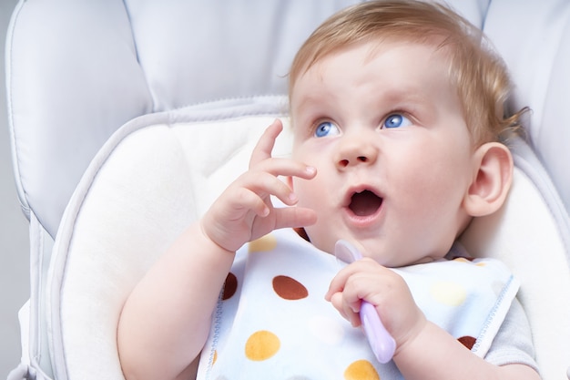 Cute baby in a child seat eats porridge. First lure Close up