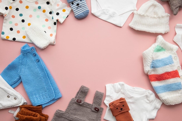 Cute baby clothes layout on a pastel pink background