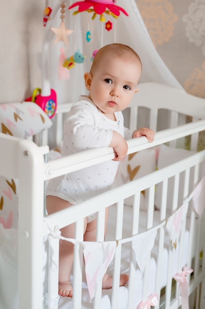 Cute baby girl 8 months sits in baby bed at home