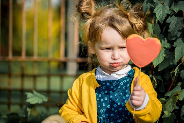 Cute baby girl in autumn park eating lollipop.