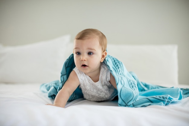 Cute baby girl under the blanket on bed in bedroom