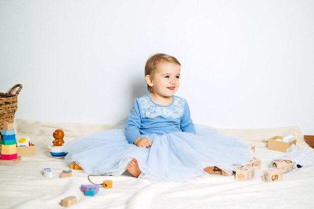 Cute baby girl in blue princess dress playing with toys at home Kids dresses for prom and birthday holiday