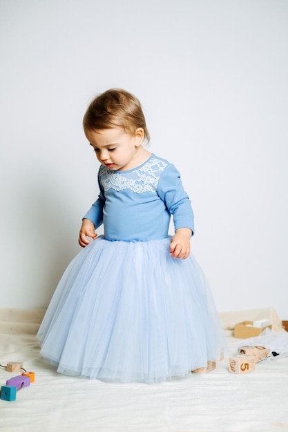 Cute baby girl in blue princess dress playing with toys at home Kids dresses for prom and birthday holiday