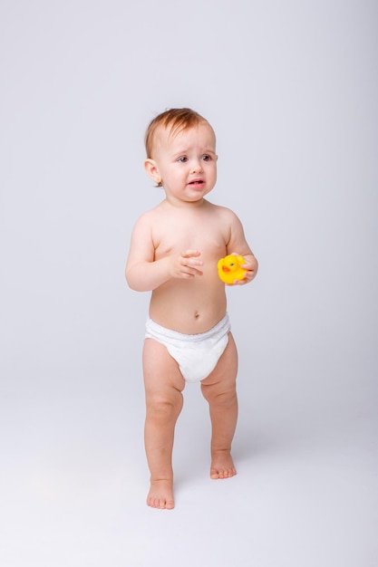 Cute baby girl in a diaper playing with a rubber toy duck isolated on a white background