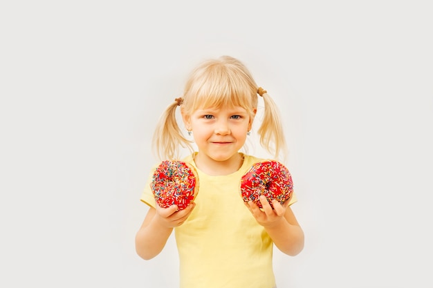 Фото Милая девочка ест сладкие пончики на светлом фоне.