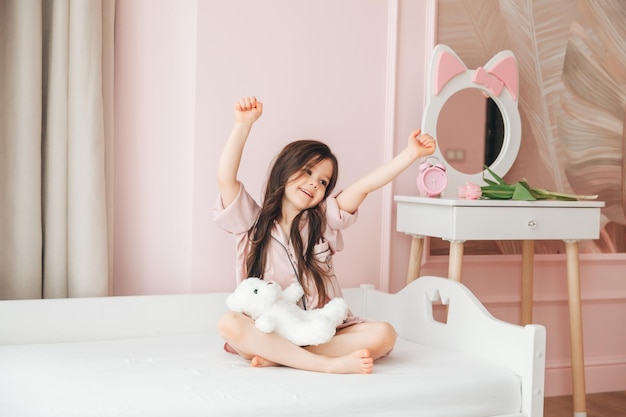 A cute baby girl enjoys a sunny morning Good morning at home A baby girl wakes up on a bed with a teddy bear