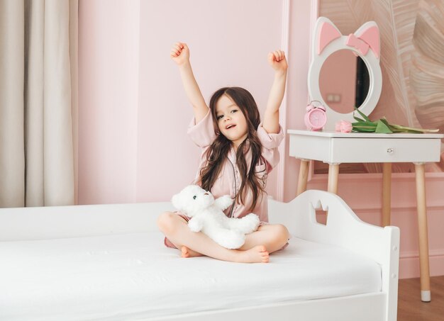 A cute baby girl enjoys a sunny morning Good morning at home A baby girl wakes up on a bed with a teddy bear