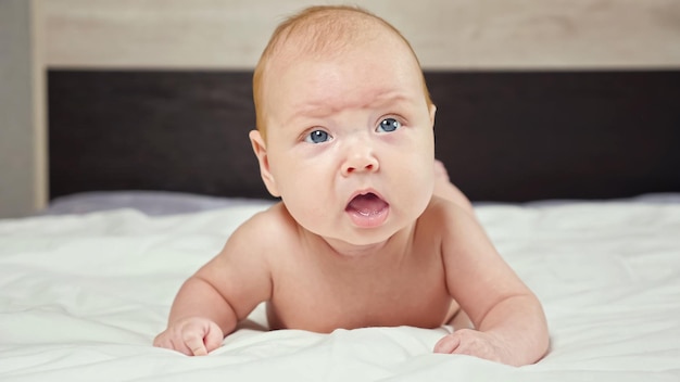 Cute baby girl frowns trying to raise up head lying on bed