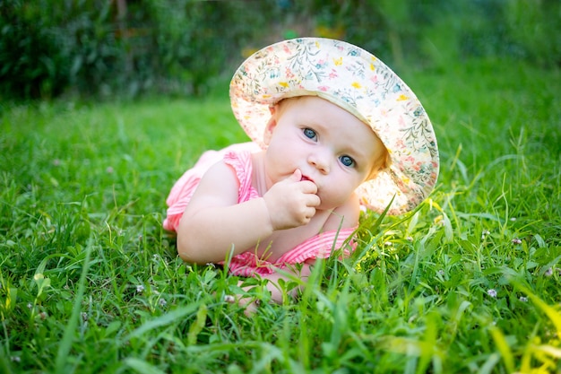 帽子をかぶって太陽の下で夏の緑の芝生の上のかわいい女の赤ちゃん