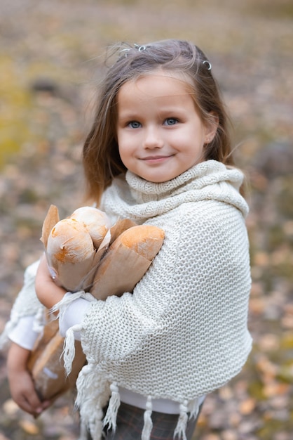 Cute baby girl holding baguettes in an autumn park on a warm day